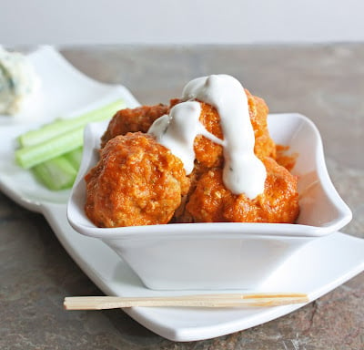 Keto Buffalo chicken meatballs in a square white dish garnished with celery and a drizzle of blue cheese dressing.