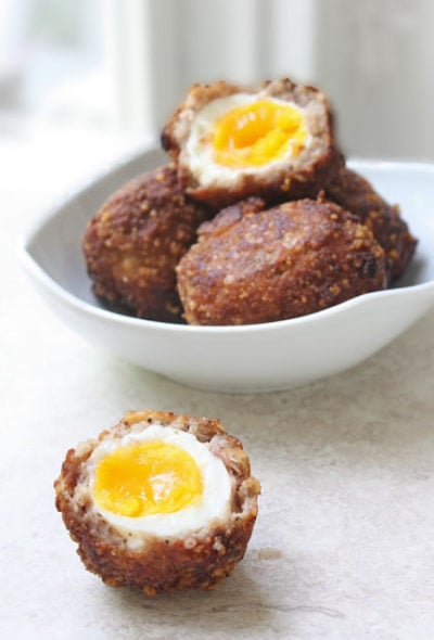 Bowl of scotch eggs with one cut in half to show soft yolk inside