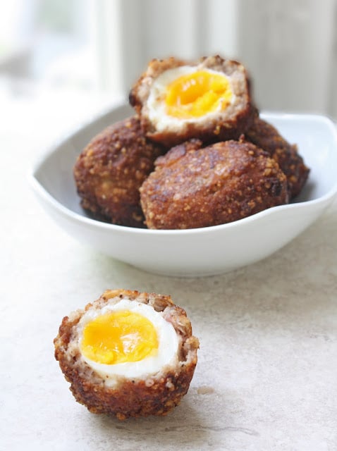 Keto scotch eggs in a white bowl with one cut in half to show the soft yolk.