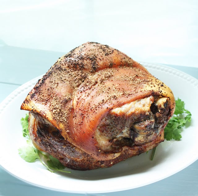 whole roasted pork shoulder with crispy skin on a white platter
