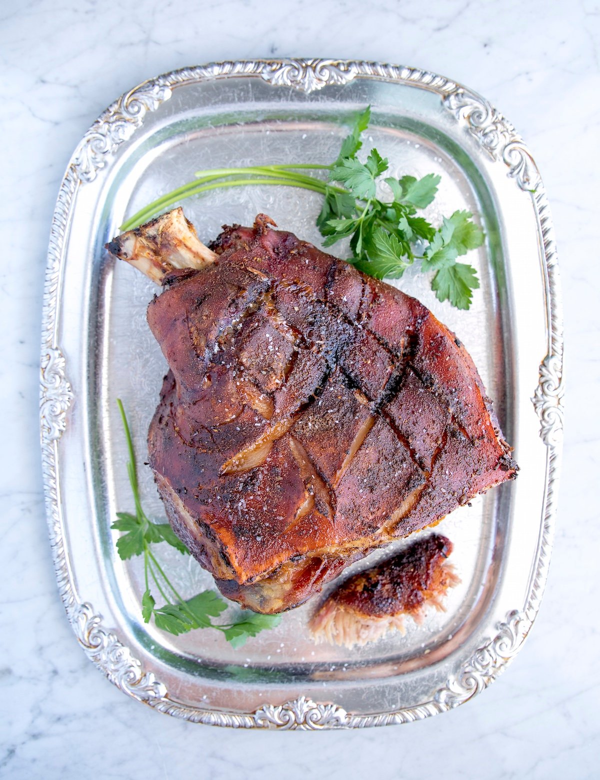 easy roasted pork shoulder with the bone in on a silver platter garnish dwith cilantro