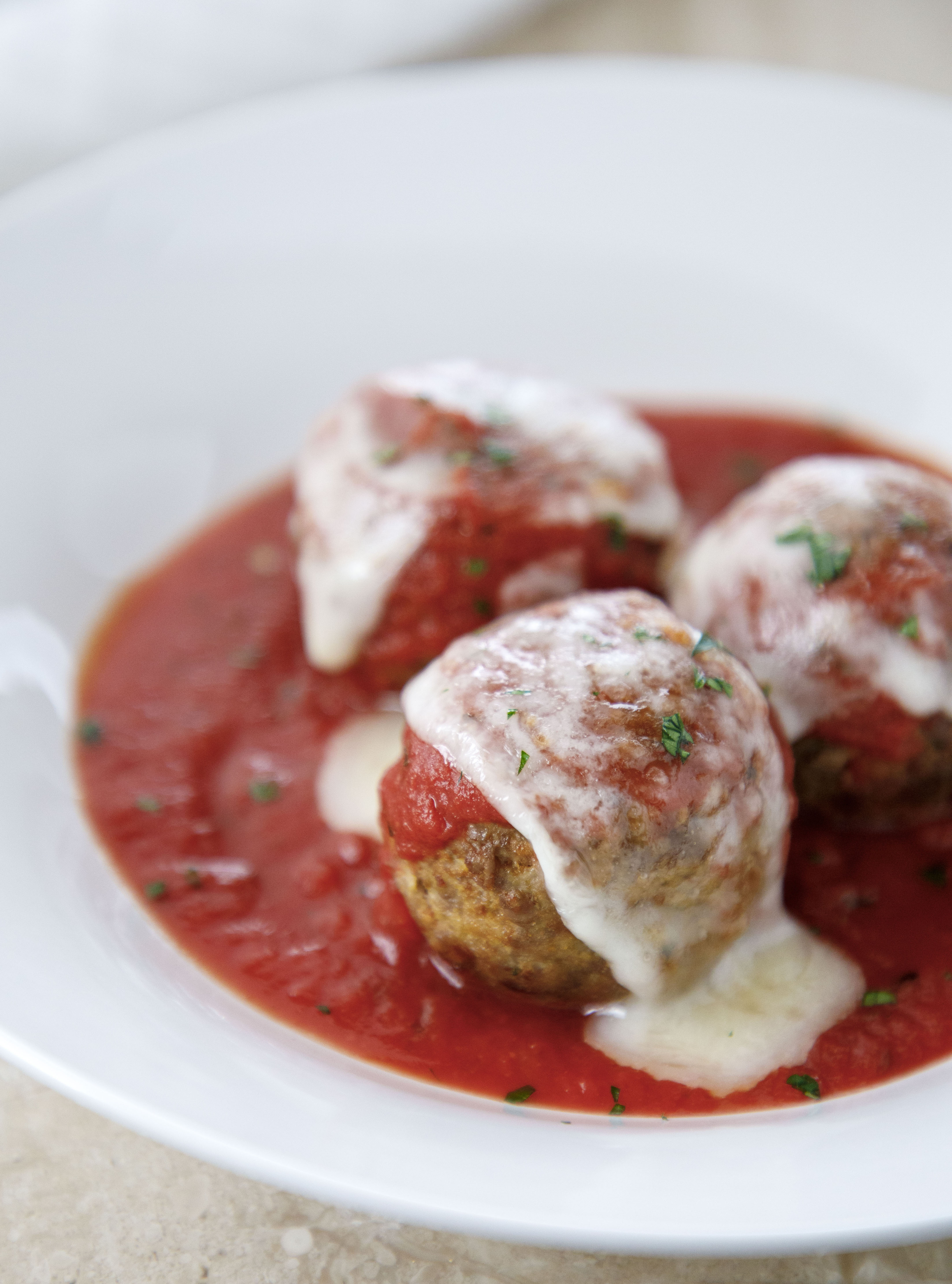 keto meatballs parmigiana on a white plate with marinara sauce and melted mozzarella cheese.
