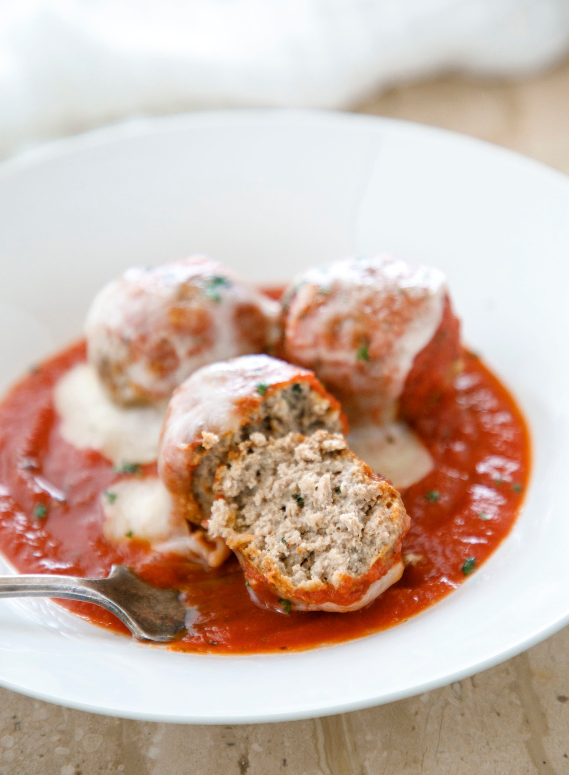Bowl of keto meatballs with one cut in half and in marinara sauce with melted mozzarella cheese.