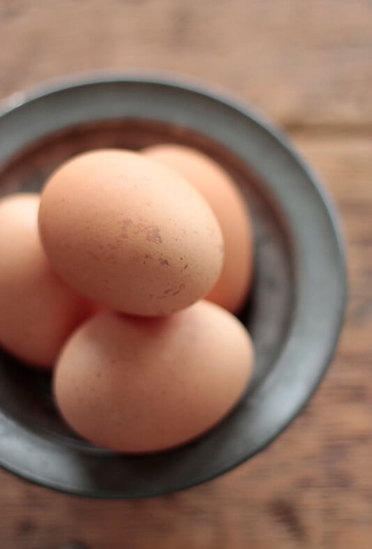 brown speckled eggs in a pewter bowl on a wooden table