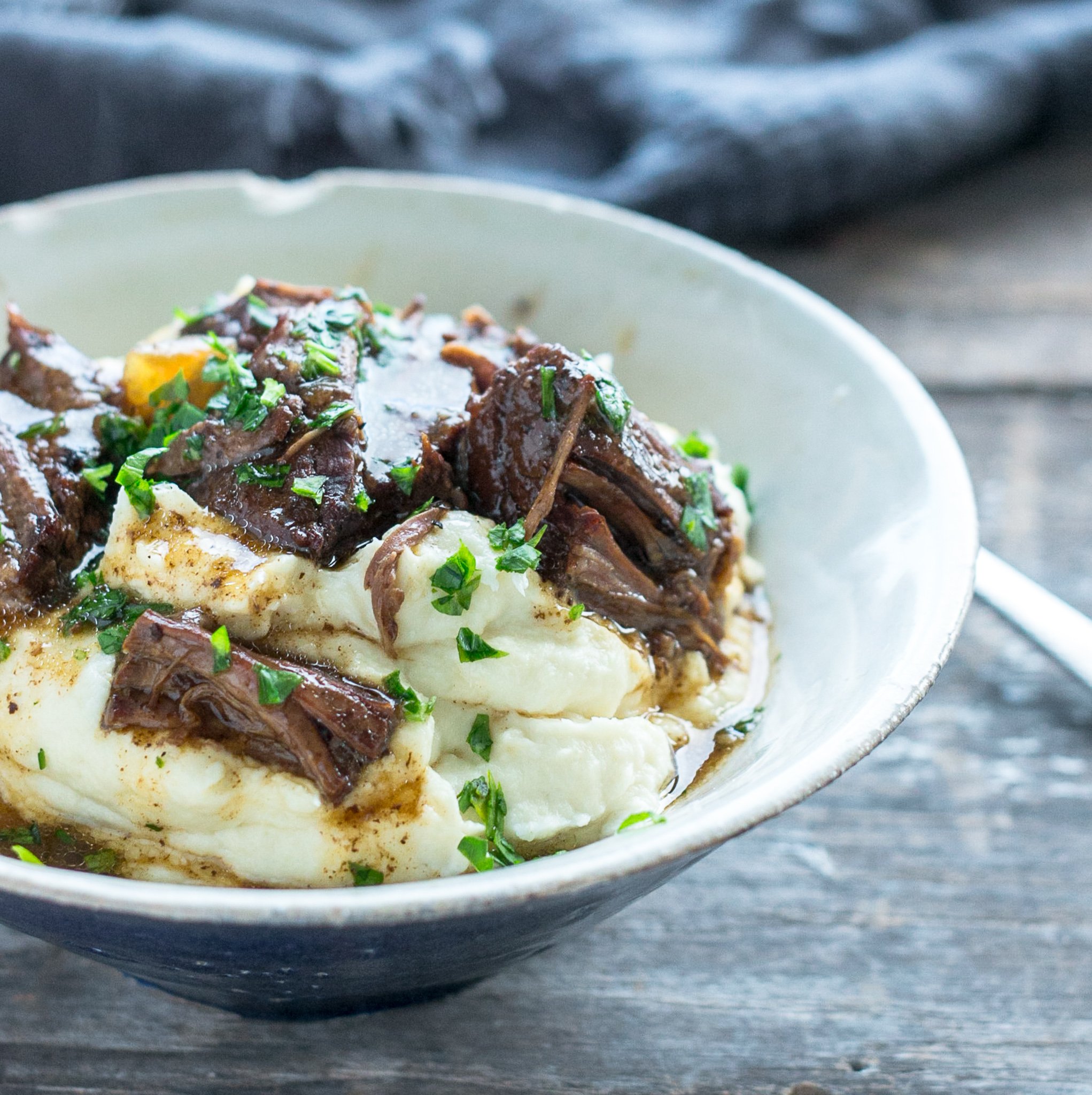side view of keto beef pot roast in a blue and white bowl with cauliflower puree