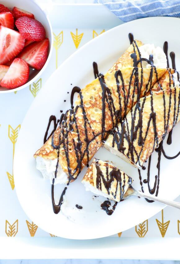 Keto Cannoli Stuffed Crepes with chocolate drizzle and bowl of strawberries