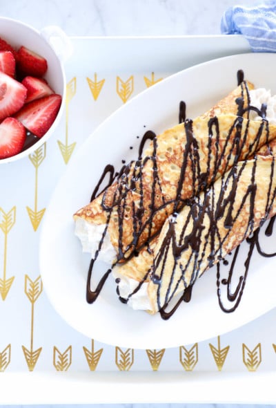 Keto Cannoli Stuffed Crepes on white tray with gold arrows
