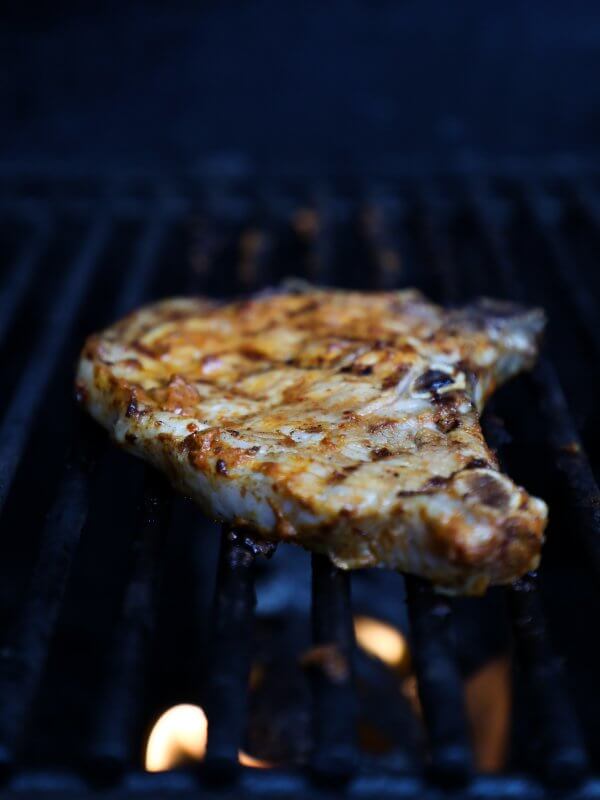 Keto Pork Chops al Pastor - Pork chop cooking on grill with flames