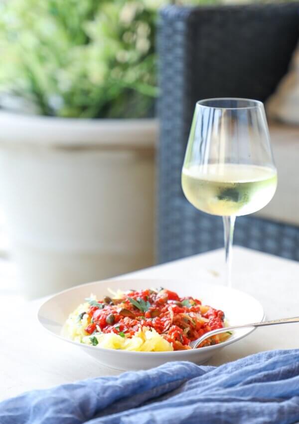 Keto Spaghetti Squash Puttanesca on a patio table with white wine