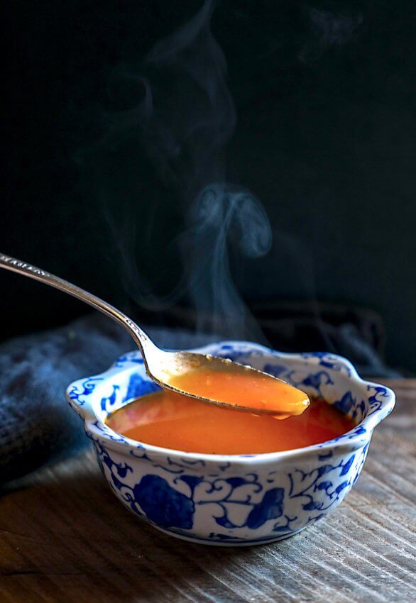 keto roasted tomato & garlic soup spoonful with steam against black background