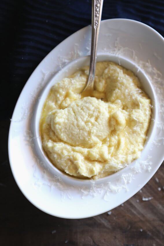 An oval white bowl of cheesy keto polenta shot from above with a spoon in it.