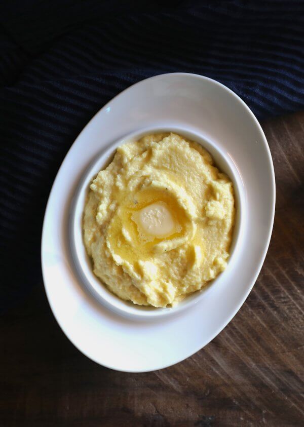 A white oval bowl filled with cheesy Keto polenta and a pat of butter on top