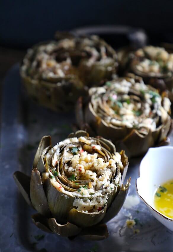 Keto Stuffed Artichokes on a platter with melted butter in a white bowl