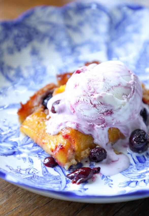 Keto Peach and Blueberry Slab Pie on a blue and white plate with a scoop of mixed berry ice cream on top