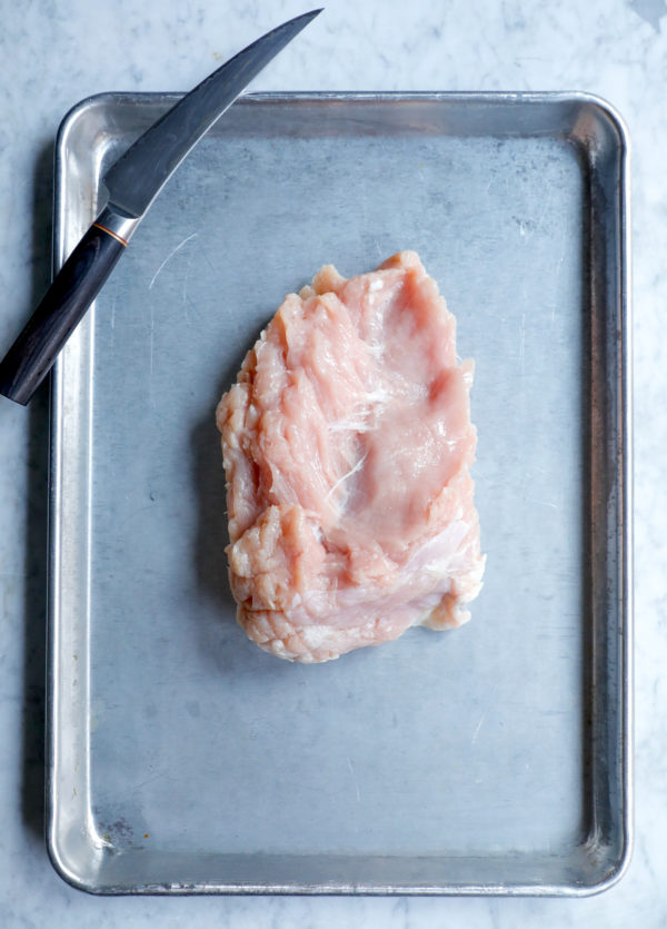 Raw turkey breast shown skin side down on a baking sheet before trimming