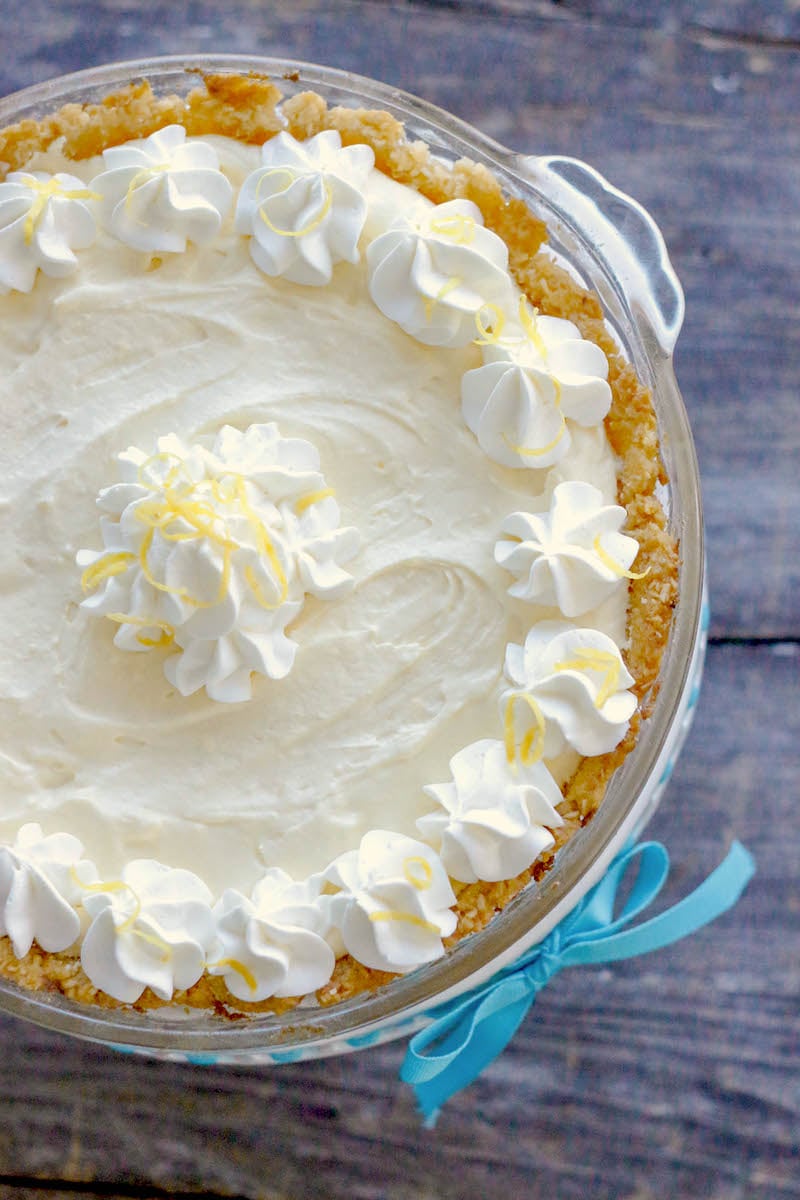 Keto Lemon Pie in a clear glass pie plate garnished with whipped cream rosettes and grated lemon zest