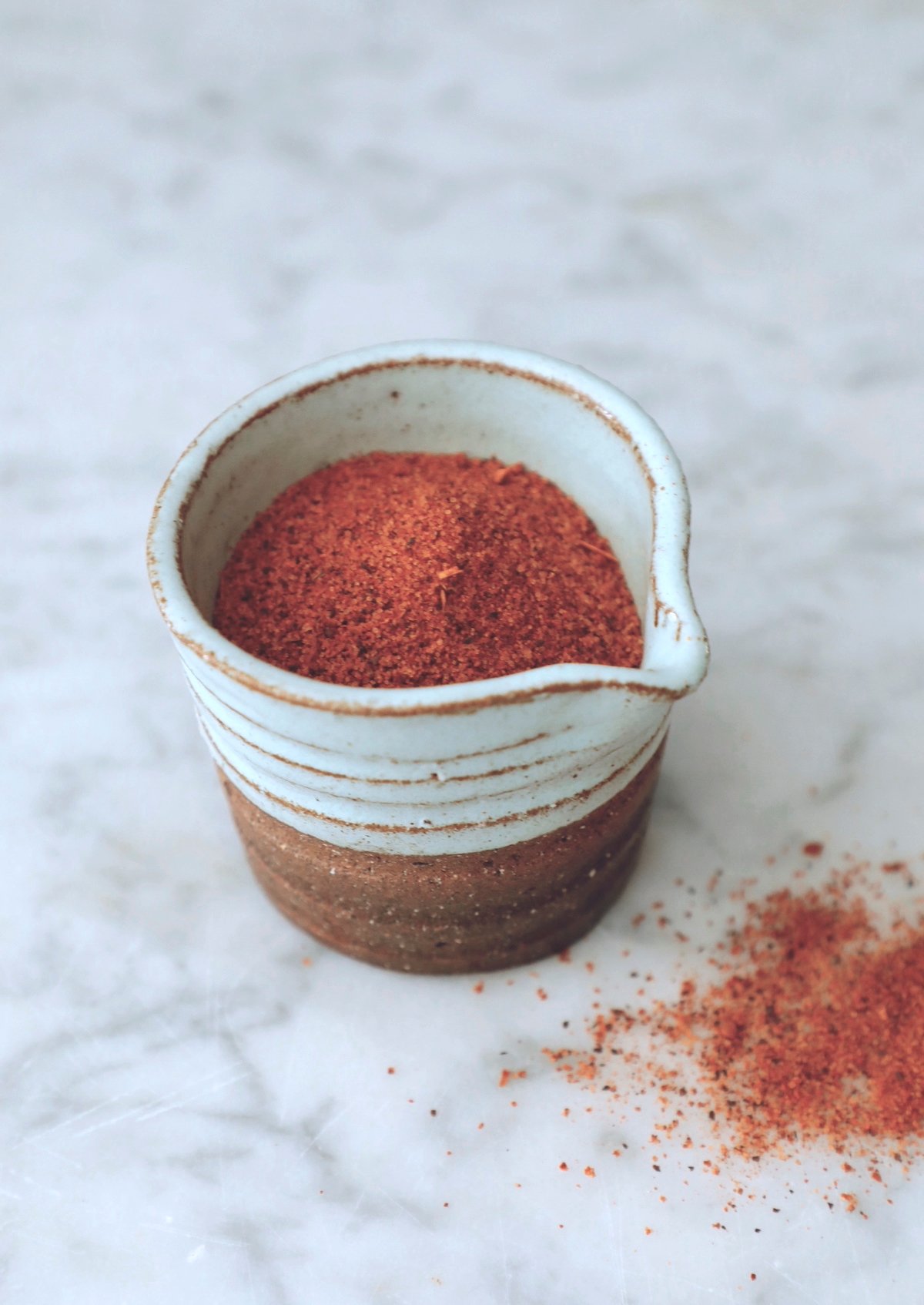 A small aqua pottery jar full of cajun seasoning on a white marble background