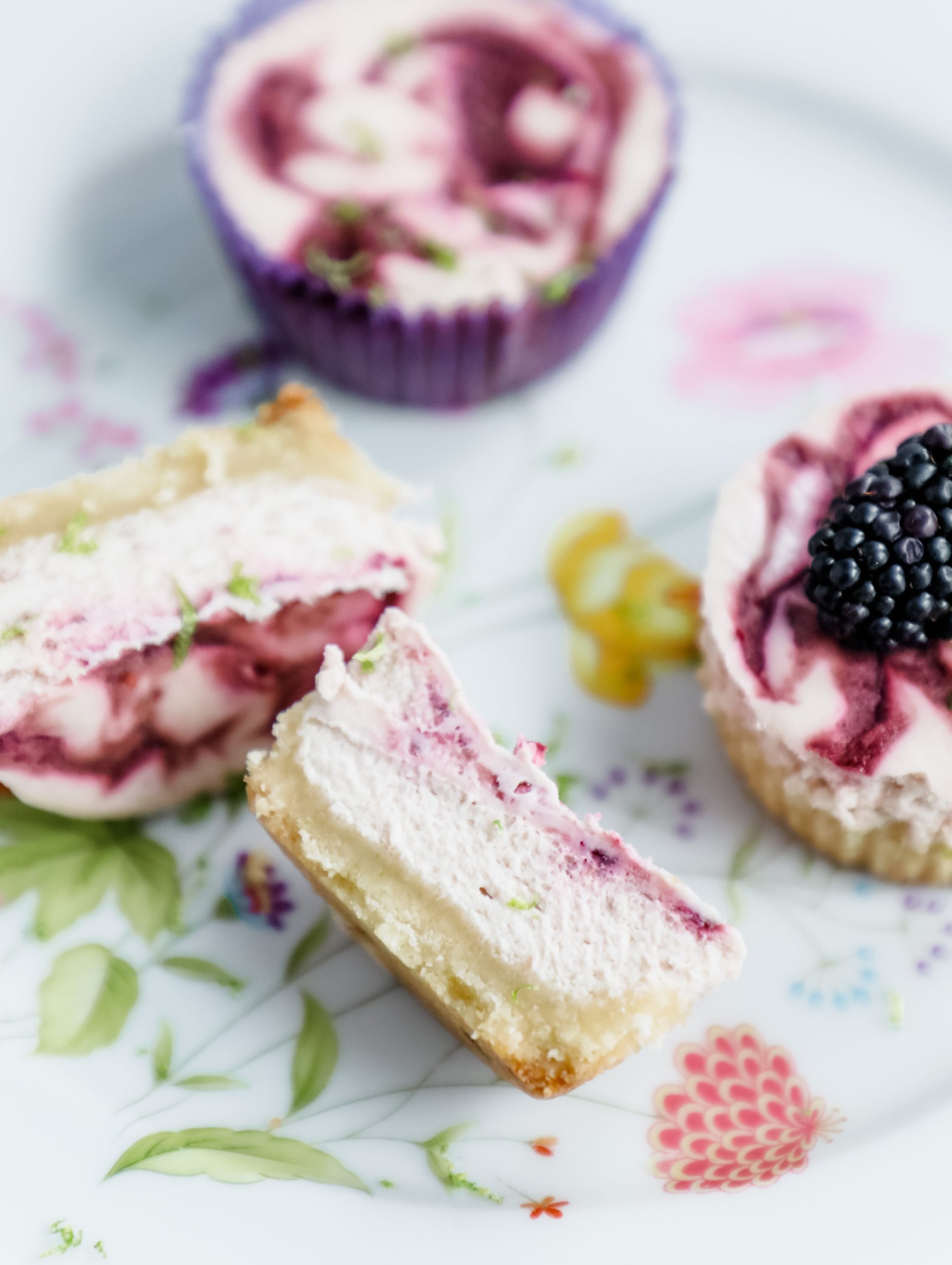 Cross section of blackberry lime cheesecakes on a flowered plate