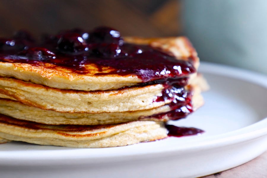 squeaky clean keto pancakes stacked with a blueberry compote drizzling down the side