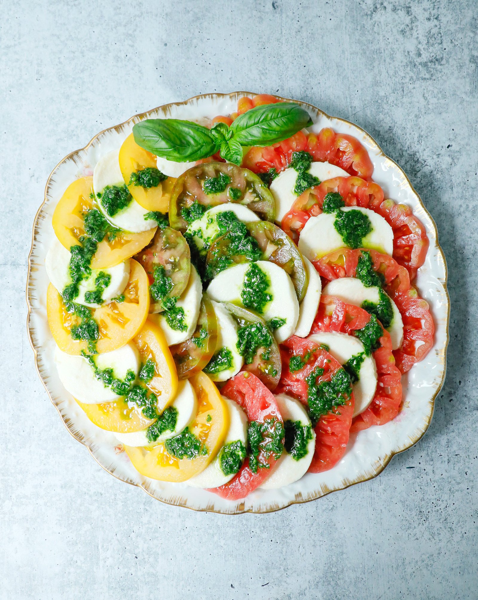Top view of a caprese salad using green, yellow and red tomatoes on a round platter.
