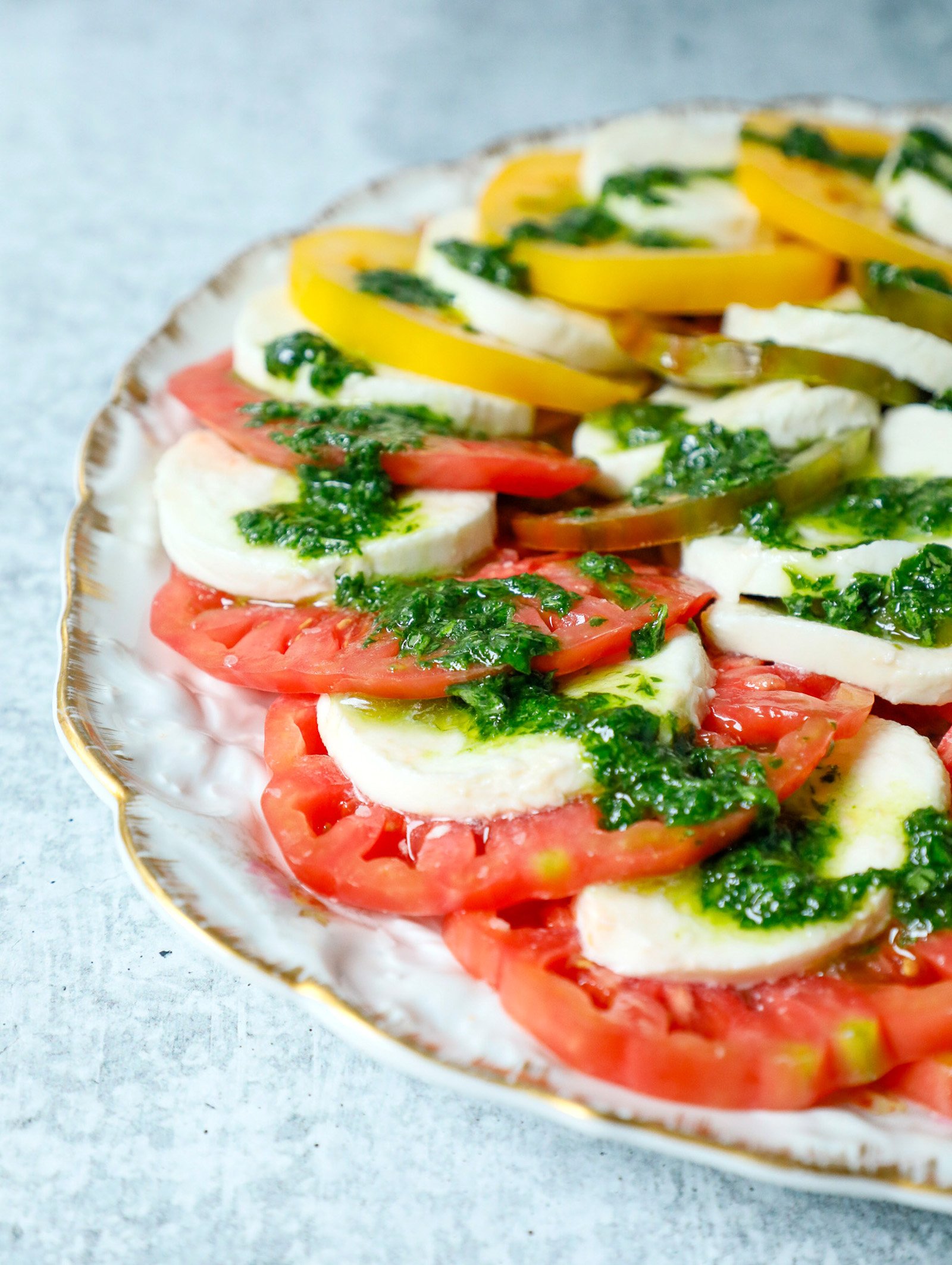 Front view of a caprese salad showing layers of red and yellow tomato with slices of fresh mozzarella and drizzled with basil oil.
