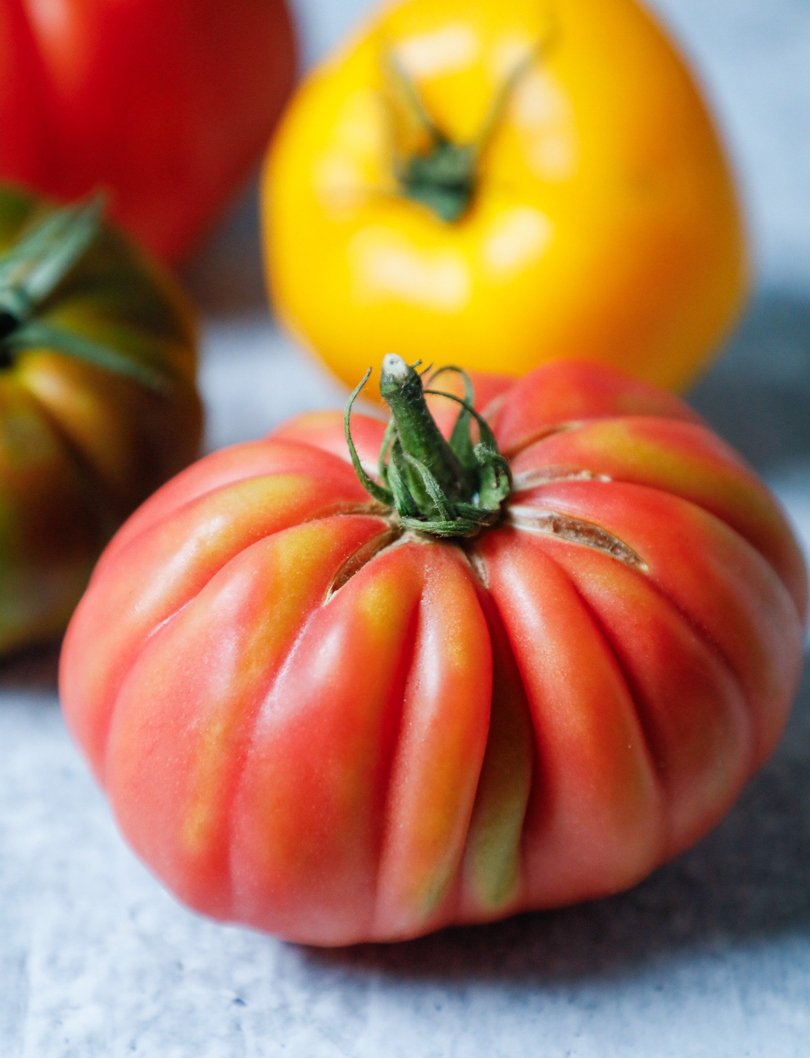 Heirloom tomatoes shown whole in multiple colors on a concrete background.
