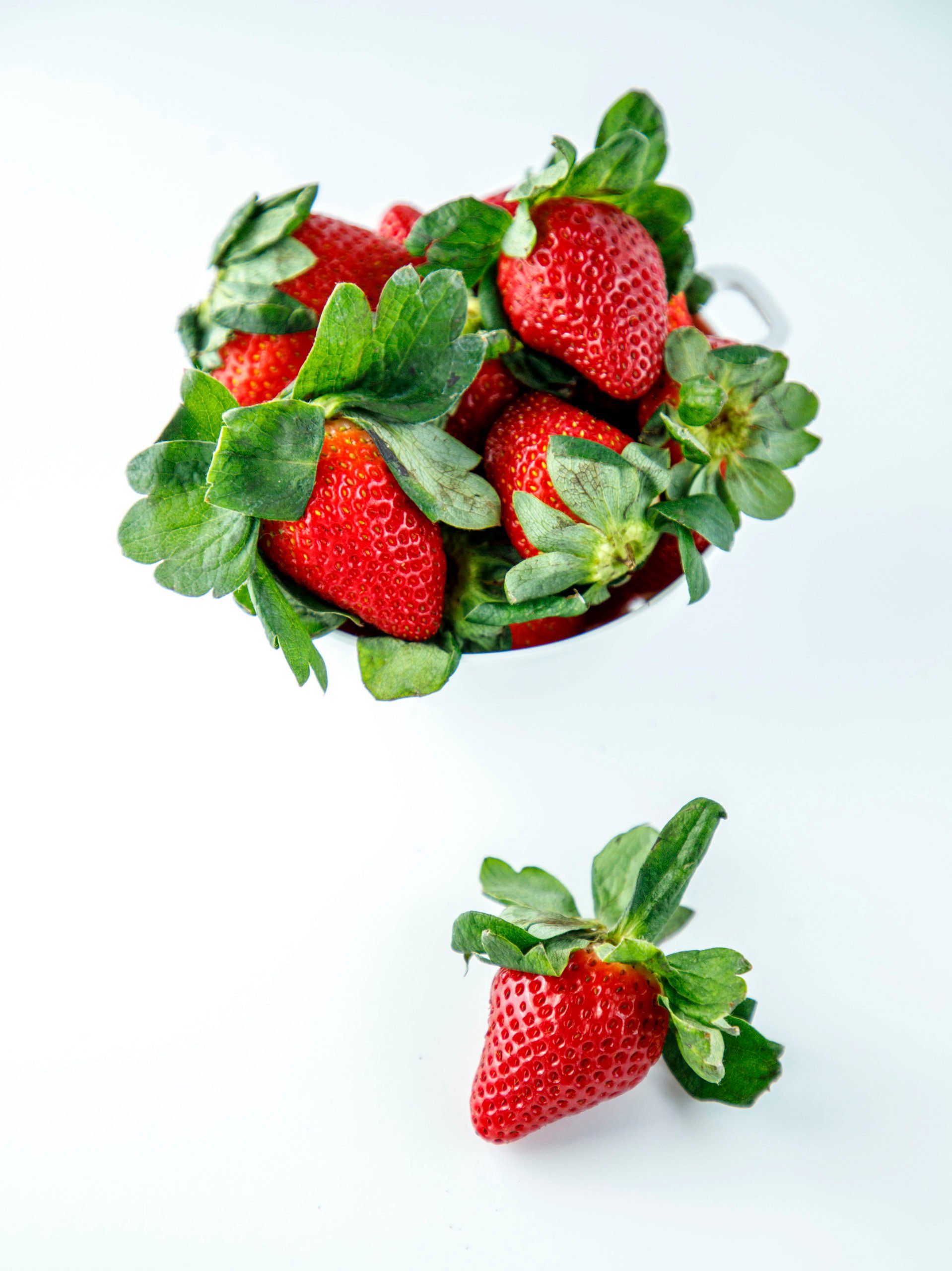 Fresh strawberries in a white colander on a white background