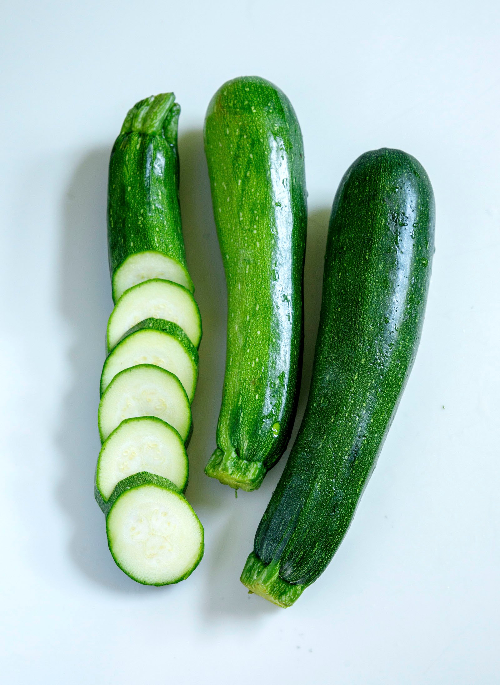 Three zucchini on a white background, one of them is sliced into rounds.