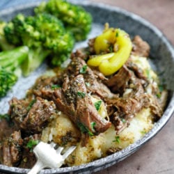 A forkful of shredded Keto Mississippi Pot Roast served over cauliflower mash on a blue enamelware plate with broccoli on the side