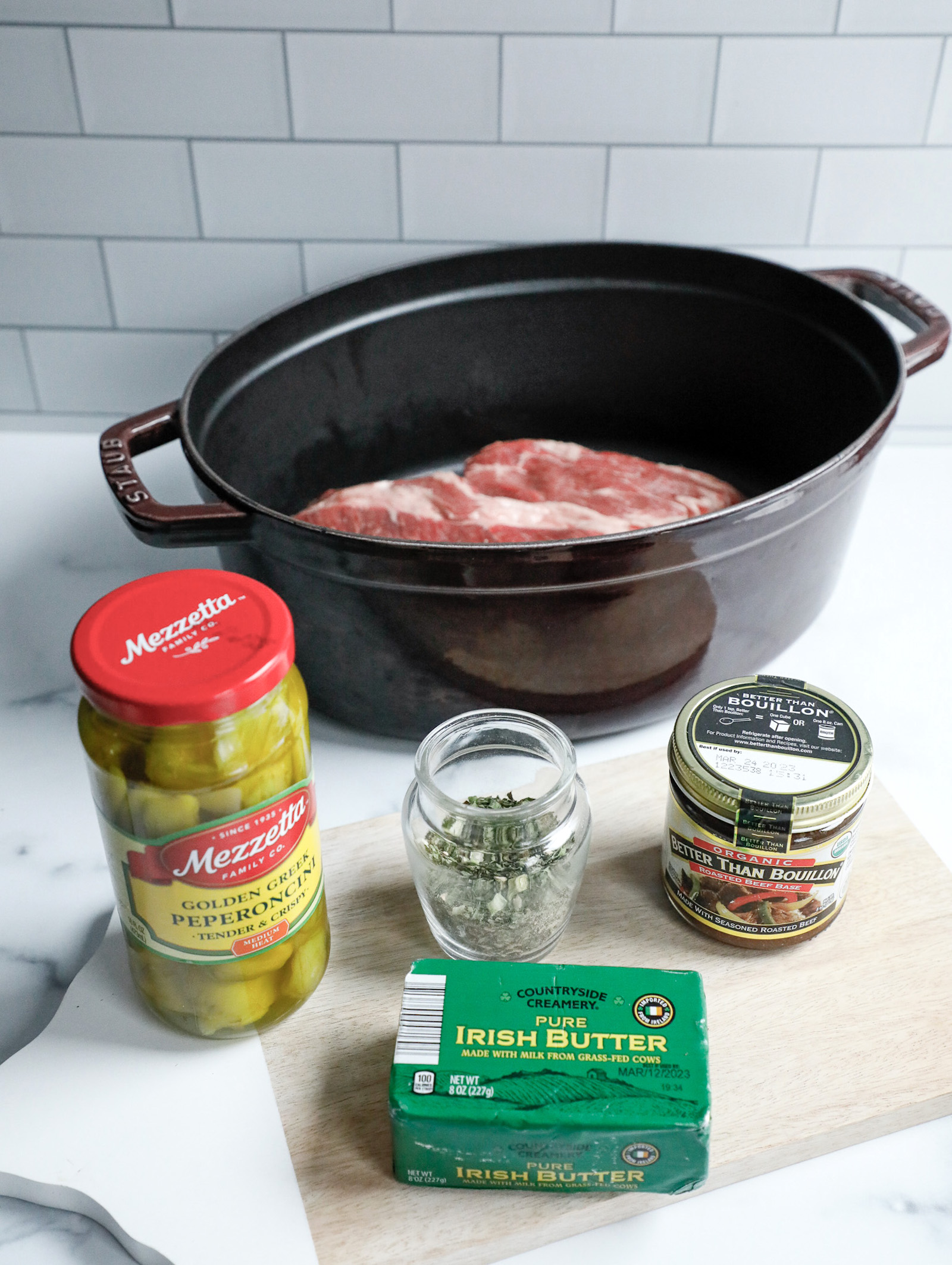 Mississippi Pot Roast Ingredients shown on a cutting board with a white subway tile backsplash in the background