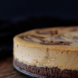 Keto pumpkin cheesecake whole, on a wooden serving board with a dark background