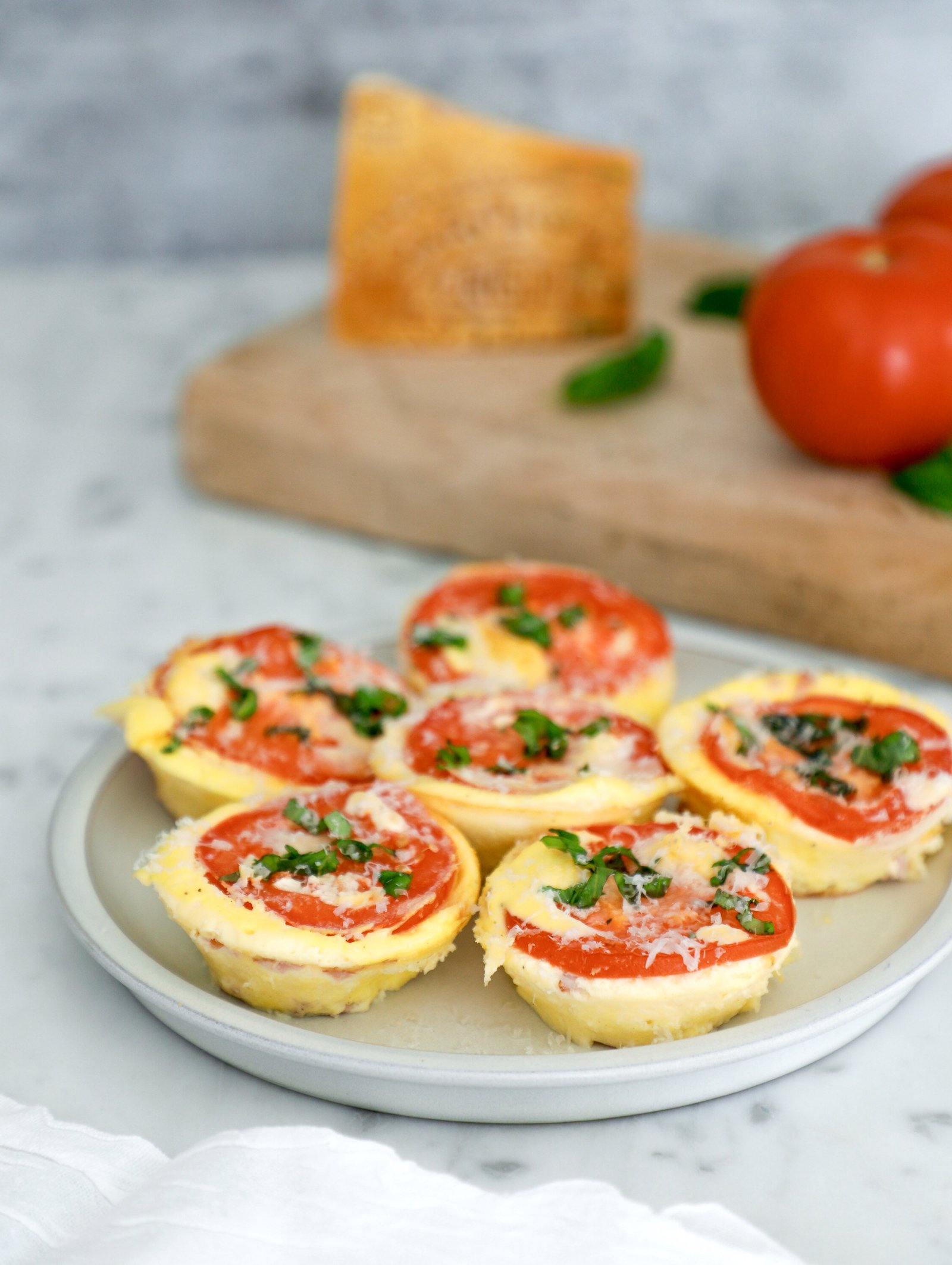High protein egg bites arranged on a grey plate with a tomato slice on top, garnished with chopped basil. 