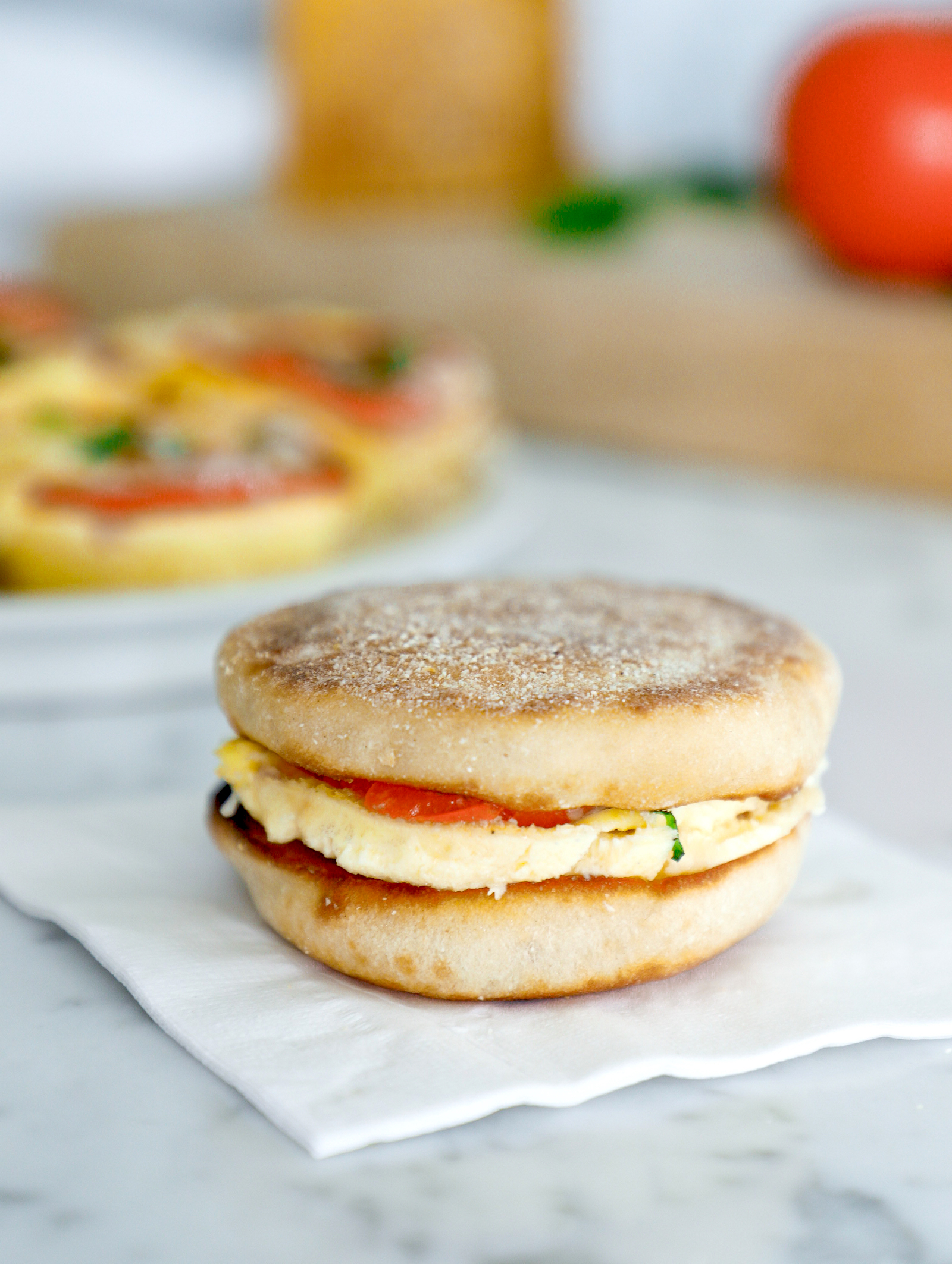 A high protein egg bite sandwiched between two halves of a toasted English muffin on a white napkin. 