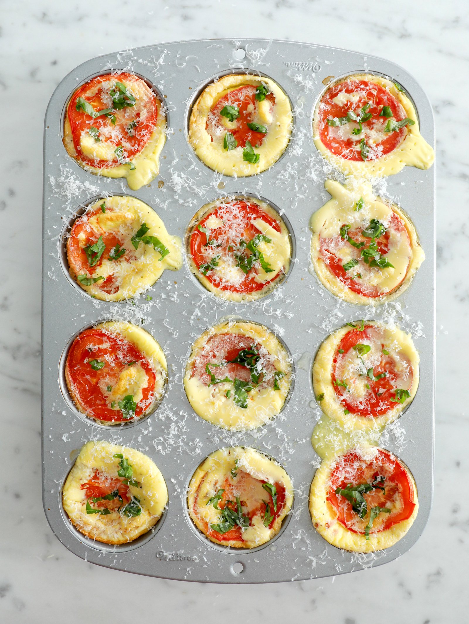 12 high protein egg bites shown cooked in a metal muffin tin and garnished with fresh basil and grated parmesan cheese