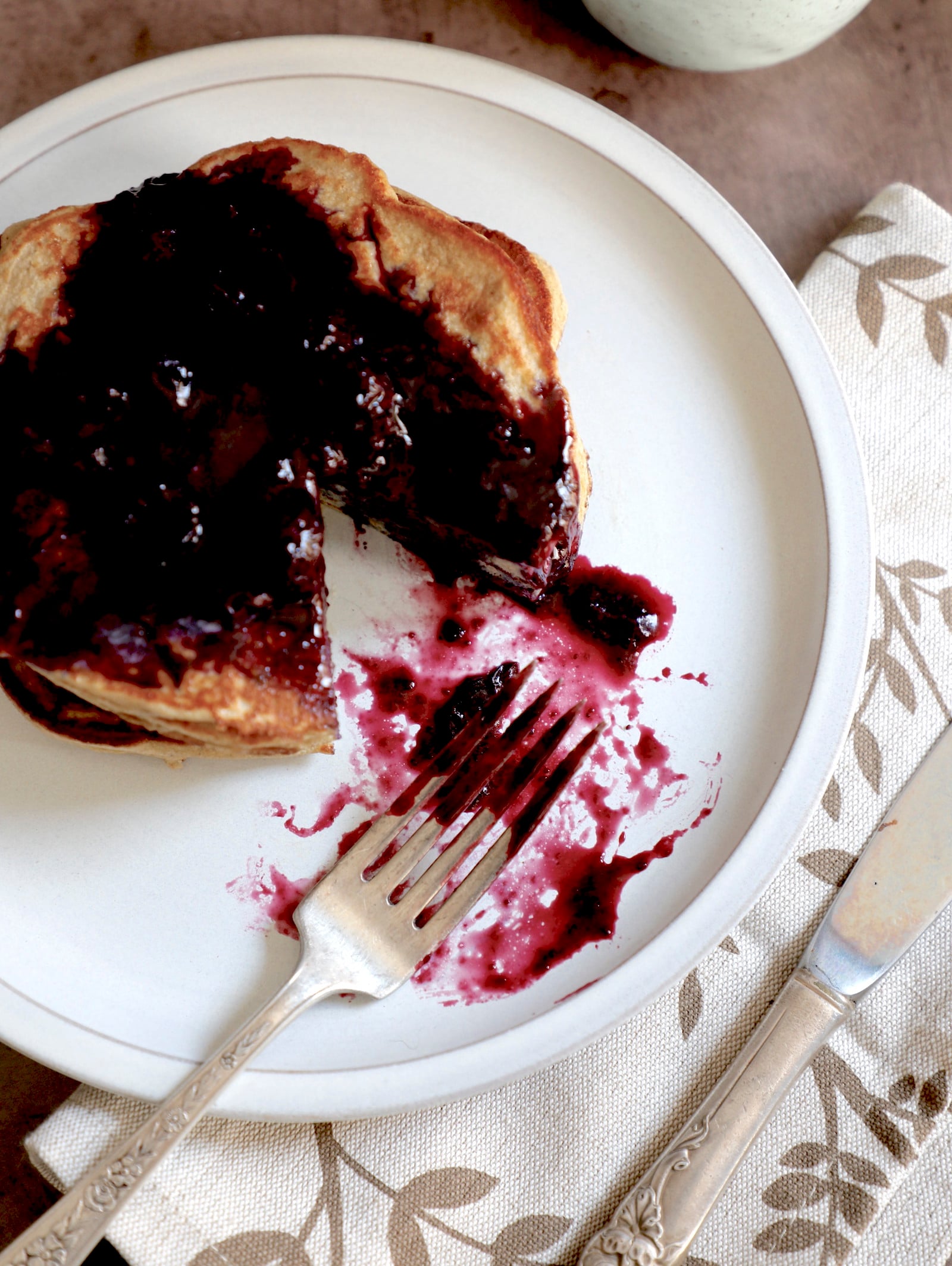 top view of pancakes on a white plate with berry compote on top and a triangle piece missing with the fork on the plate in a pool of compote.